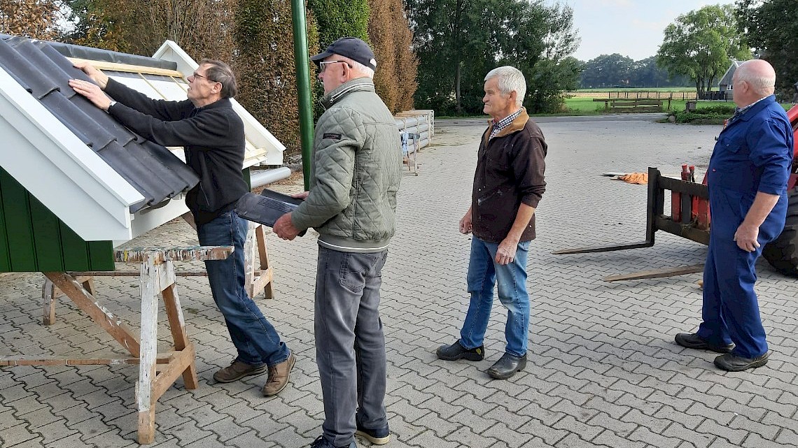 Harrie Nobbenhuis kijkt of de dakpannen passen op het bouwwerk. Henk Koorman, Gerard Grootelaar en Theo Lohuis kijken toe. Foto: Anton Schrijver.